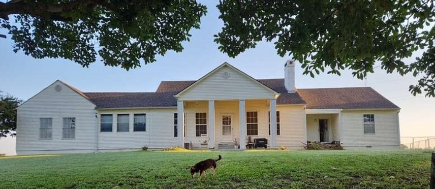 White farmhouse with its old, worn brown roof before replacement
