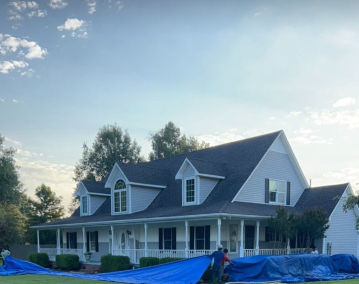 White farmhouse with tarps laid over the lawn before a Prime re-roof