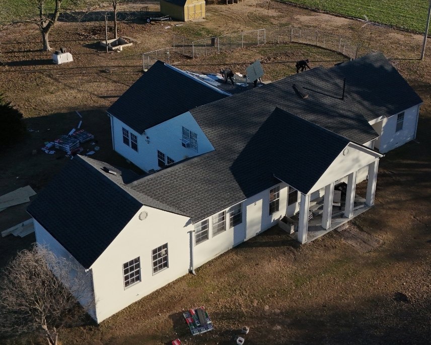 Aerial view of the same farmhouse with its finished new black shingle roof
